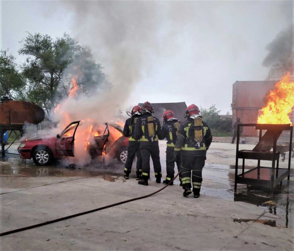 Unos bomberos apagan el fuego de un turismo.