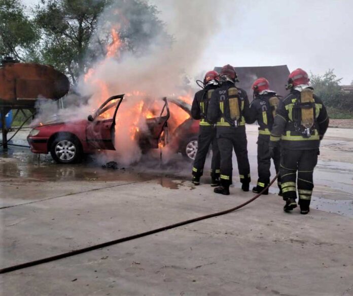 Unos bomberos apagan el fuego de un turismo.