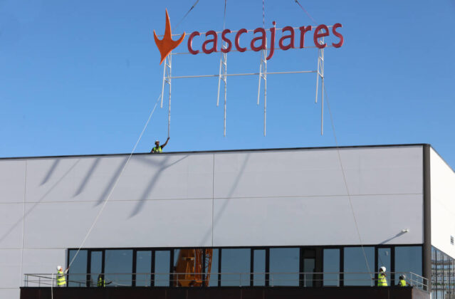 Responsables y trabajadores de Cascajares y de las empresas constructoras junto al cartel de Cascajares que sobrevivió al incendio y que se ha vuelto a recolocar en las nuevas instalaciones. / Brágimo (ICAL)