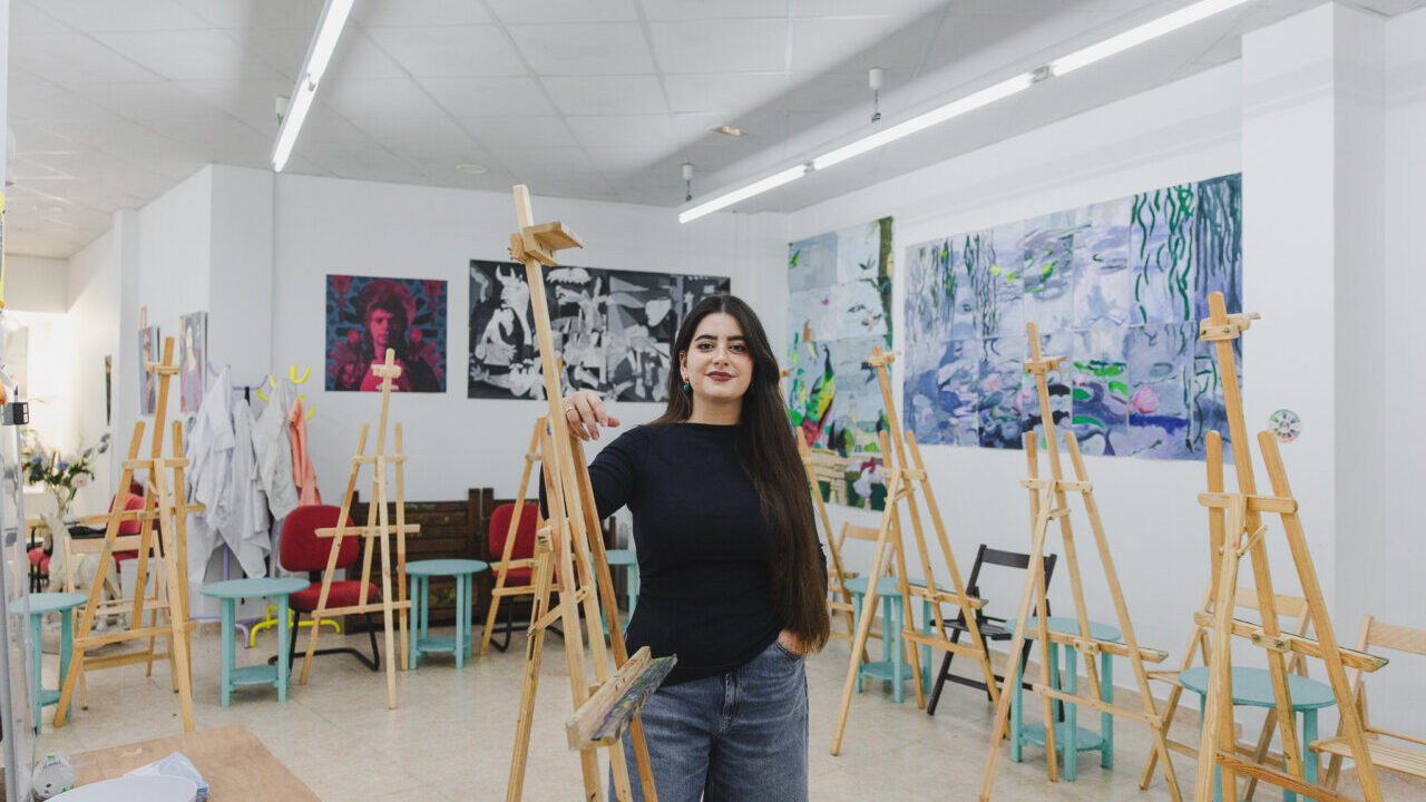 Joven pintora en su estudio rodeada de caballetes y obras de arte