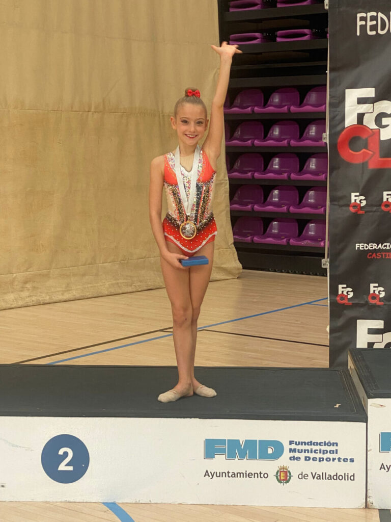 Niña gimnasta con medalla en podio tras competición de rítmica