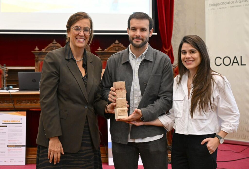 Tres personas sosteniendo un premio en un evento de arquitectura sostenible.