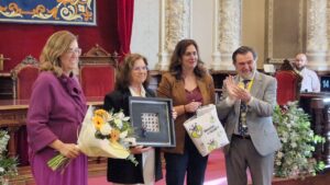 Entrega de un premio en una ceremonia con flores y un cuadro
