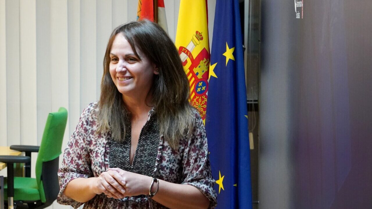 Patricia Gómez sonriente en un evento político con banderas de España y la UE