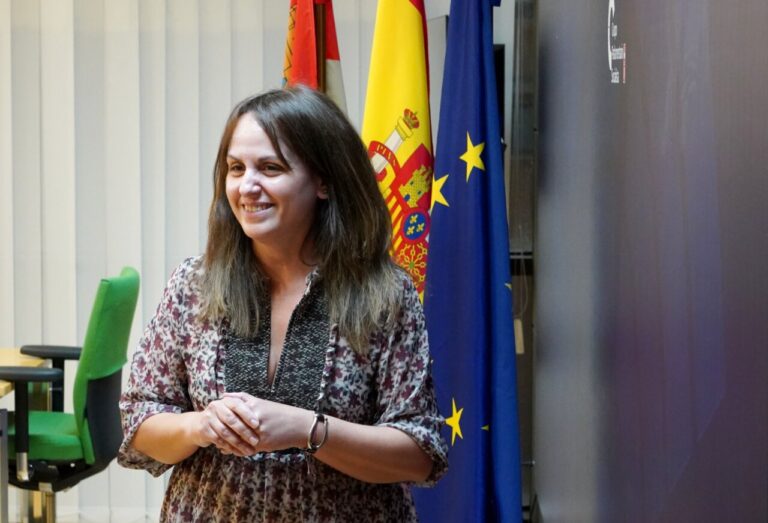 Patricia Gómez sonriente en un evento político con banderas de España y la UE