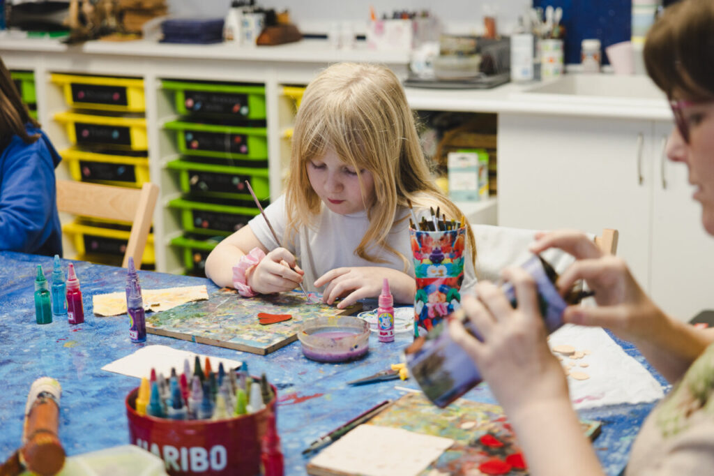 Niña pintando en un taller de cuero con otros niños.