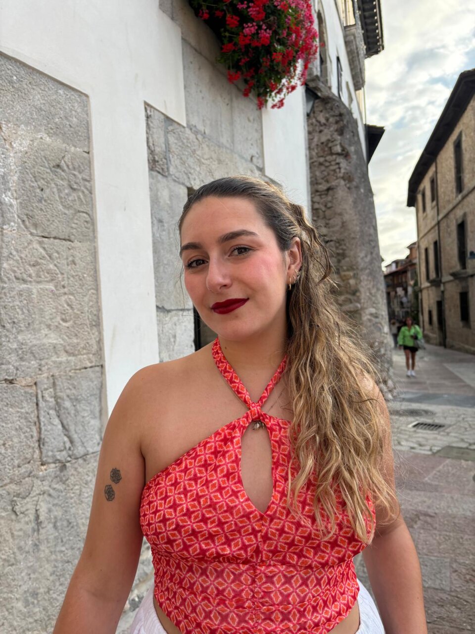 Joven mujer con blusa roja sonriente en una calle de piedra