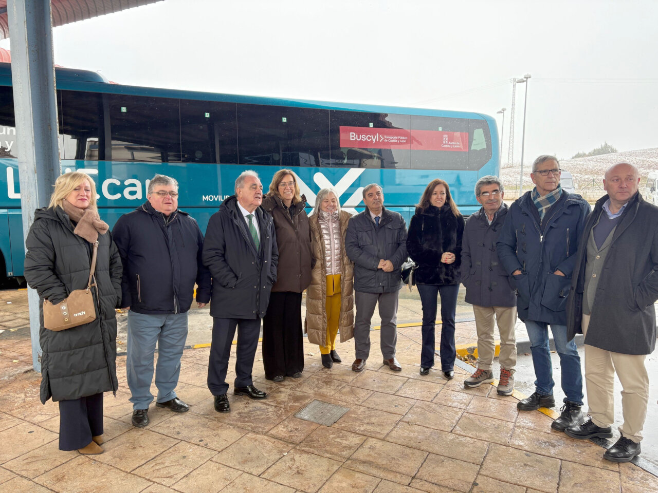 Grupo de personas en una estación de autobuses con un autobús de Buscyl