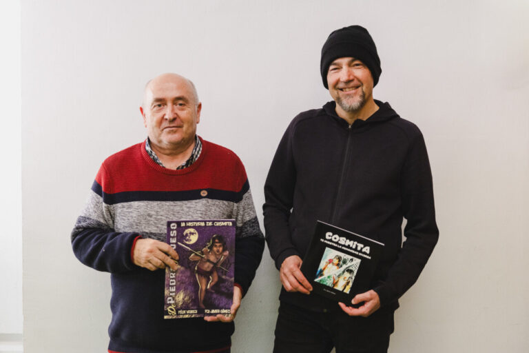 Dos hombres sosteniendo libros sobre Cosmita, un niño sordo en la Prehistoria