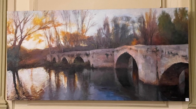 Pintura de un puente reflejado en el agua durante el atardecer