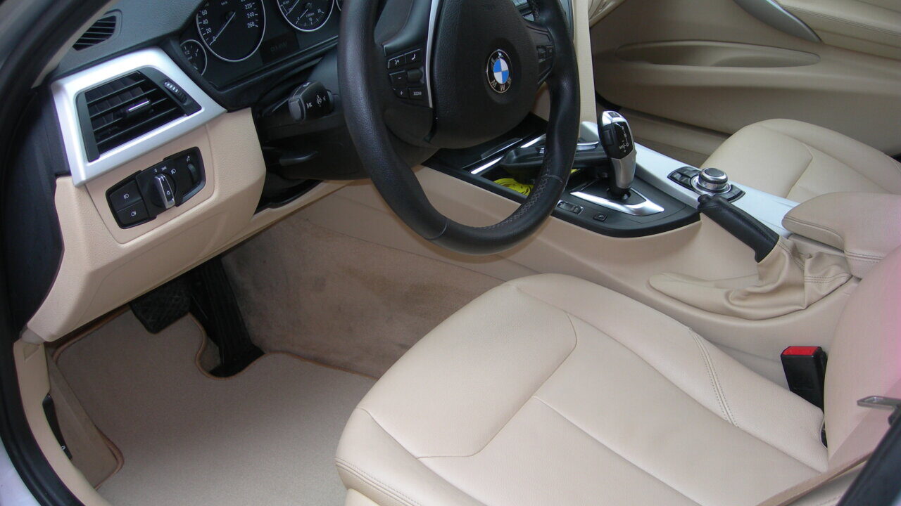 Interior de un coche con asientos de cuero claro y alfombrillas.