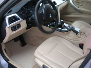 Interior de un coche con asientos de cuero claro y alfombrillas.