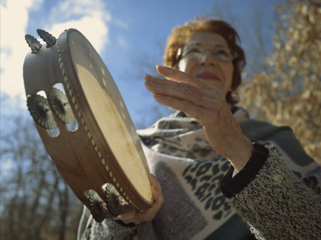 Mujer sosteniendo un pandero al aire en un entorno natural.