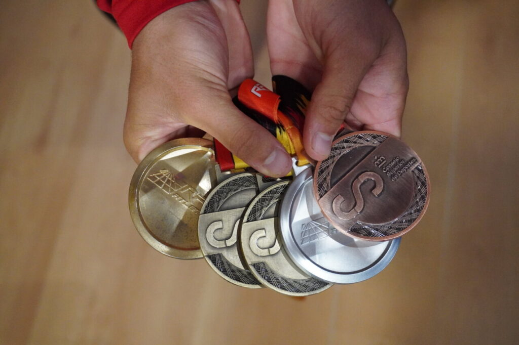 Manos sosteniendo varias medallas de atletismo en diferentes colores