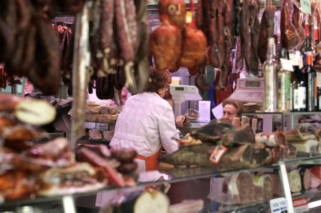 Vista de un mercado local con productos cárnicos y clientes comprando.