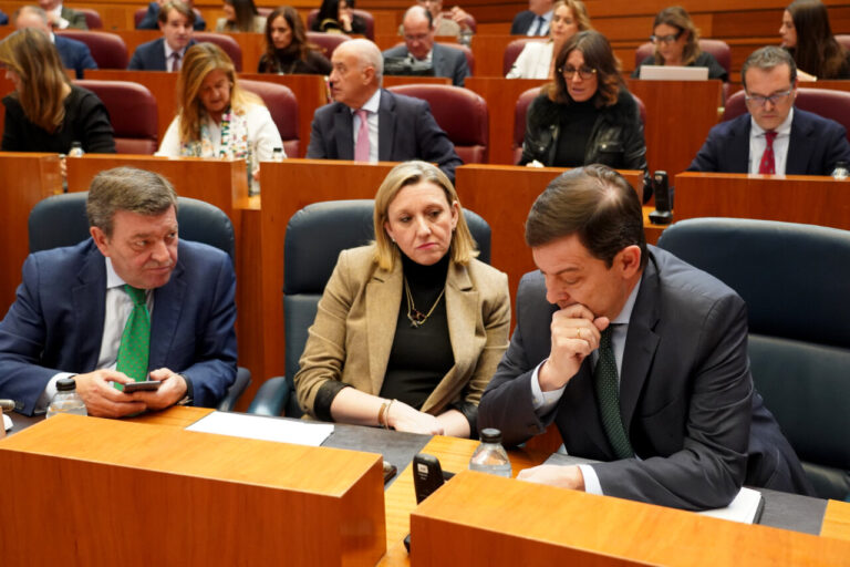 Tres personas discutiendo en una reunión sobre presupuestos en un parlamento.
