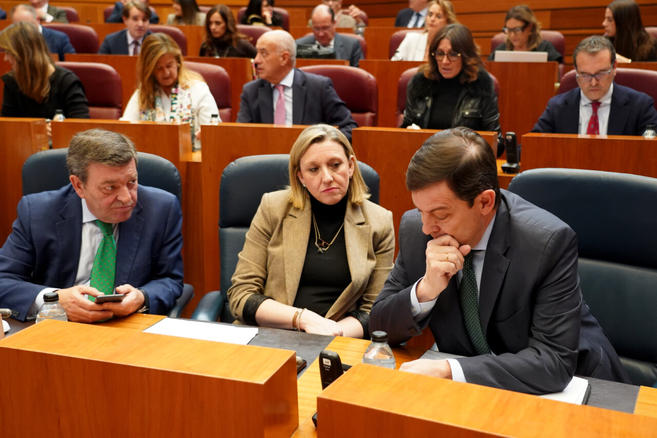 Tres personas discutiendo en una reunión sobre presupuestos en un parlamento.