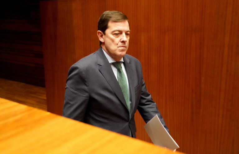 Un político camina con documentos en un entorno parlamentario.