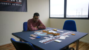 Un hombre juega a Bandas Doradas en una mesa con cartas y piezas.
