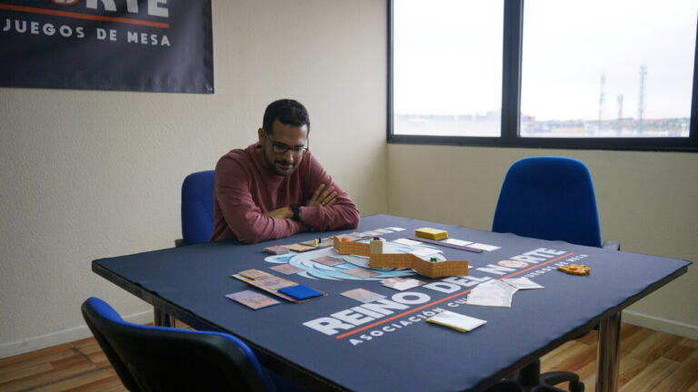 Un hombre juega a Bandas Doradas en una mesa con cartas y piezas.