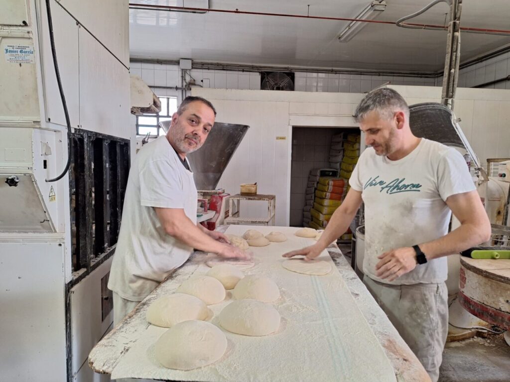 Dos panaderos trabajando la masa en un obrador tradicional.