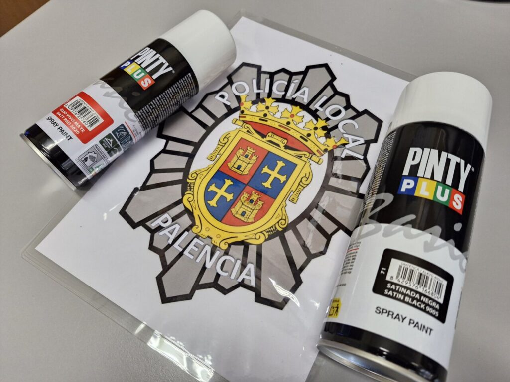 Dos botes de spray de pintura junto a un emblema de la policía local de Palencia.