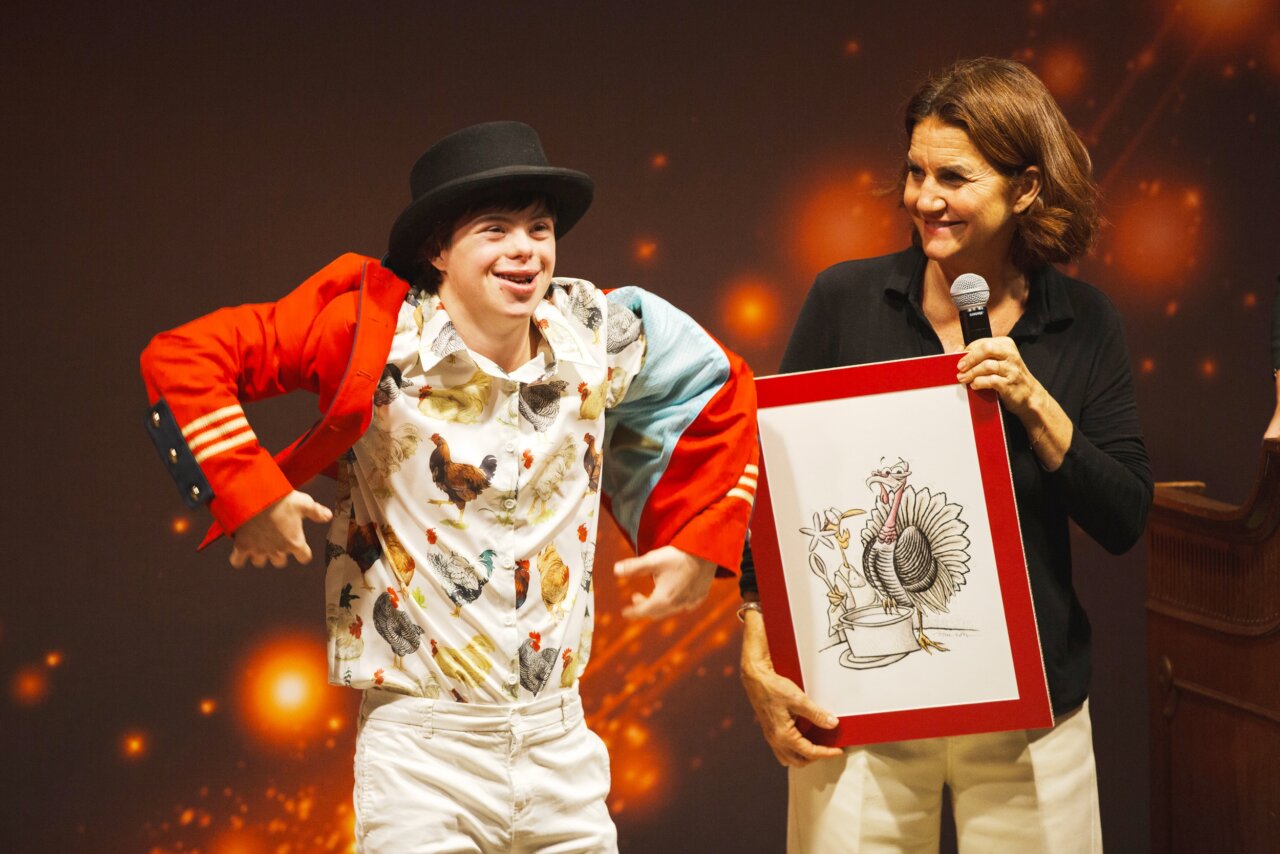 Presentador y artista sosteniendo caricatura en subasta benéfica