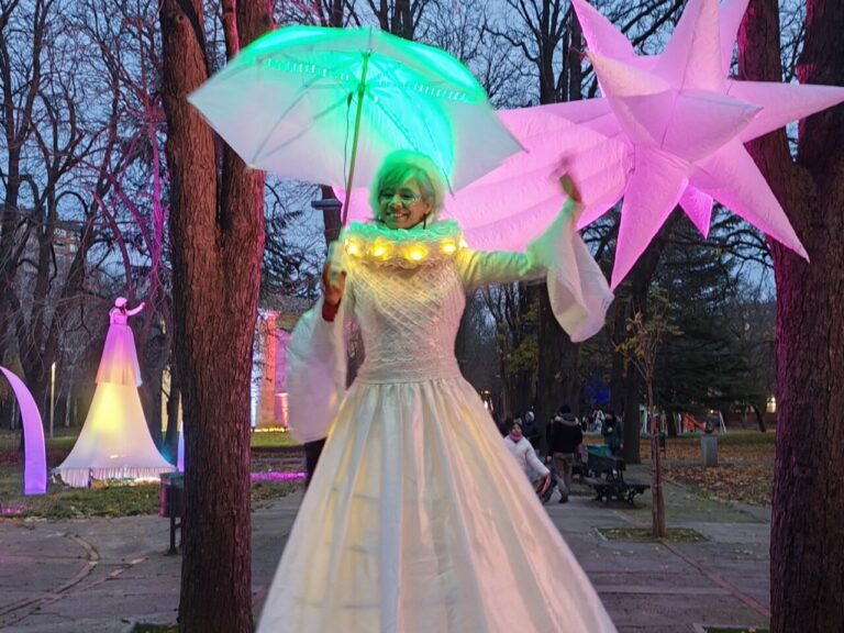 Personaje vestido de blanco con paraguas iluminado en un parque navideño