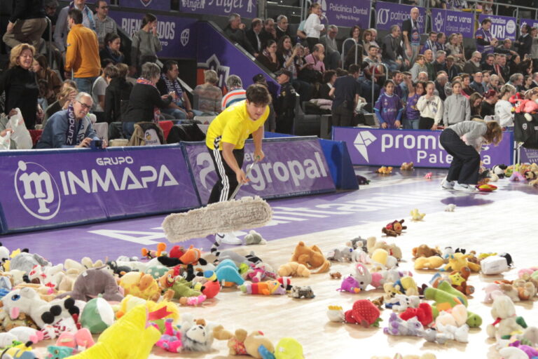 Jugadores recogen peluches en la cancha durante un evento navideño.