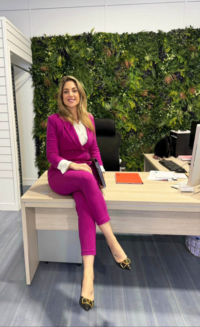 Mujer sonriente en traje rosa sentada en un escritorio moderno