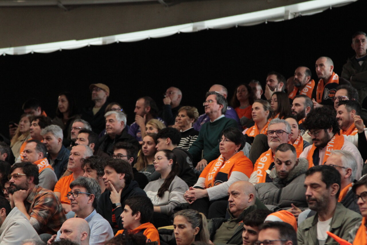 Aficionados con bufandas naranjas en un partido de baloncesto.