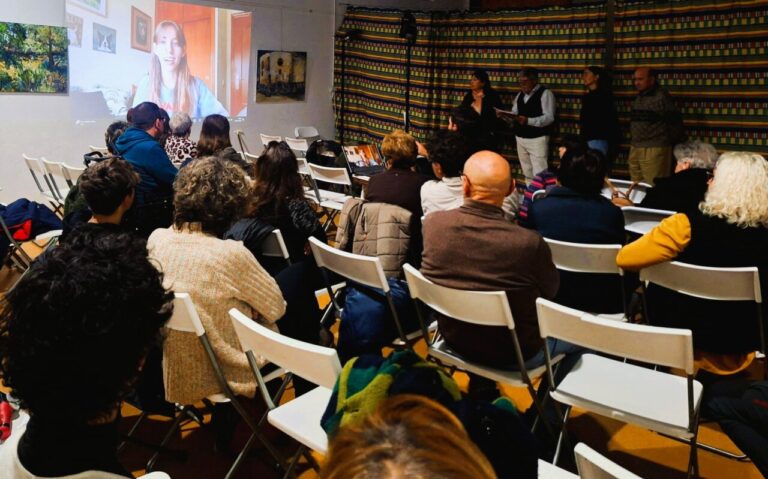 Asistentes atentos a un mensaje por videoconferencia durante un evento literario.