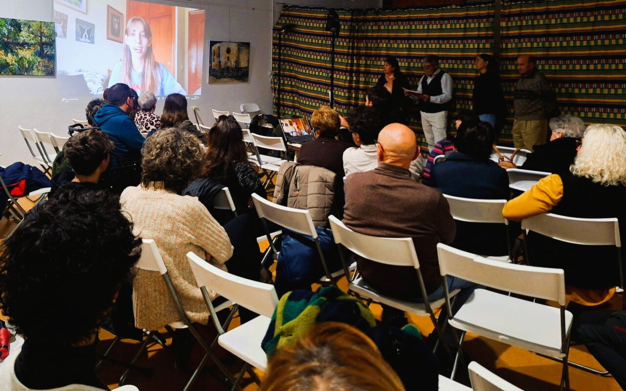 Asistentes atentos a un mensaje por videoconferencia durante un evento literario.