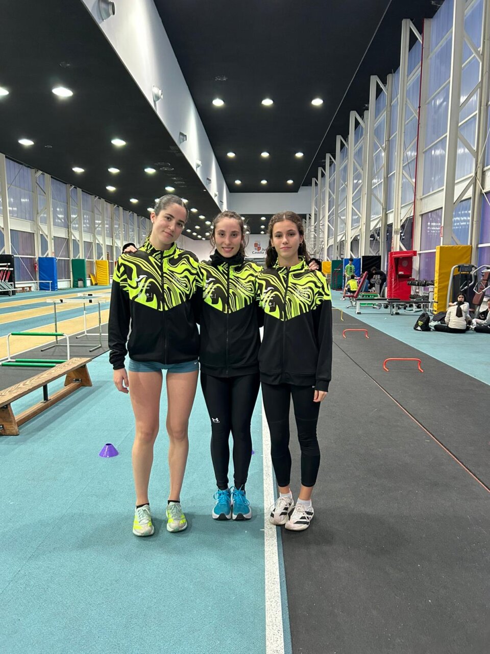 Tres atletas en un gimnasio con ropa deportiva amarilla y negra