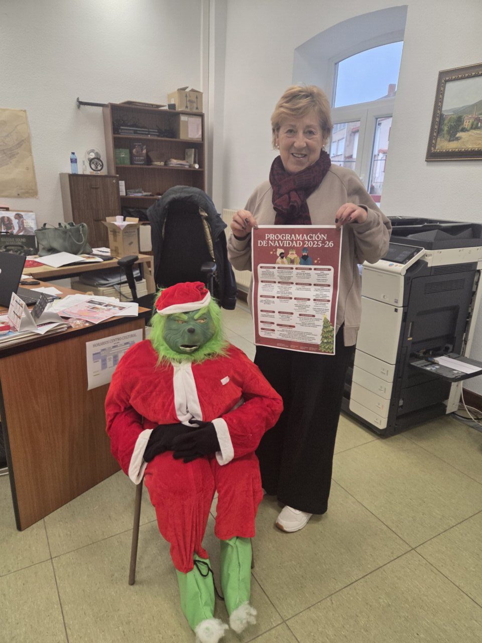 Mujer sosteniendo un cartel de programación navideña con un muñeco del Grinch.