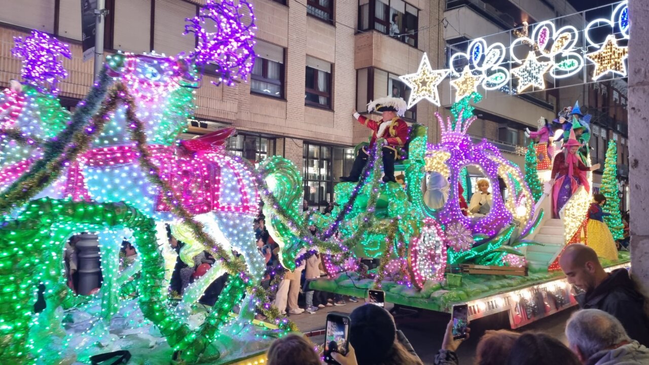 Carroza iluminada en una cabalgata navideña con personajes festivos.