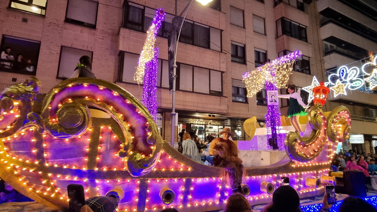 Carroza navideña iluminada con personas durante un desfile festivo.