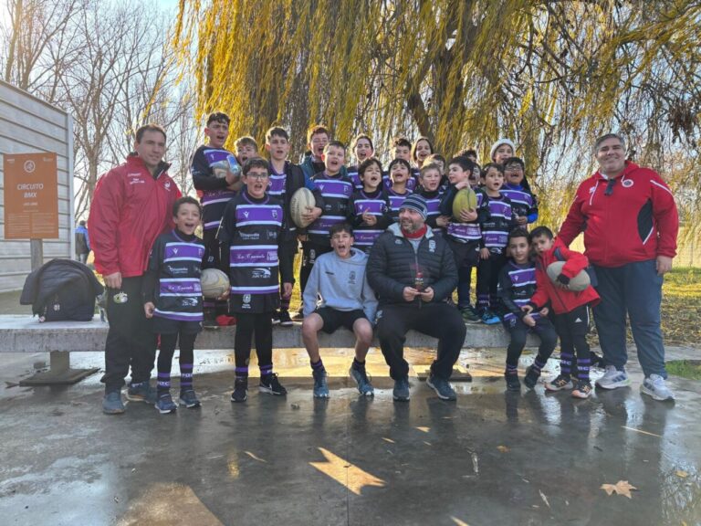 Grupo de niños de rugby posando con un trofeo en un parque