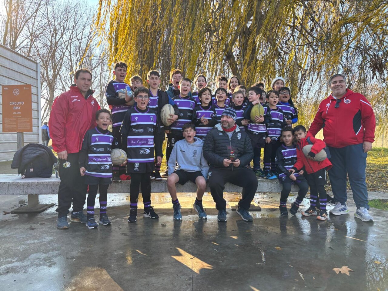 Grupo de niños de rugby posando con un trofeo en un parque