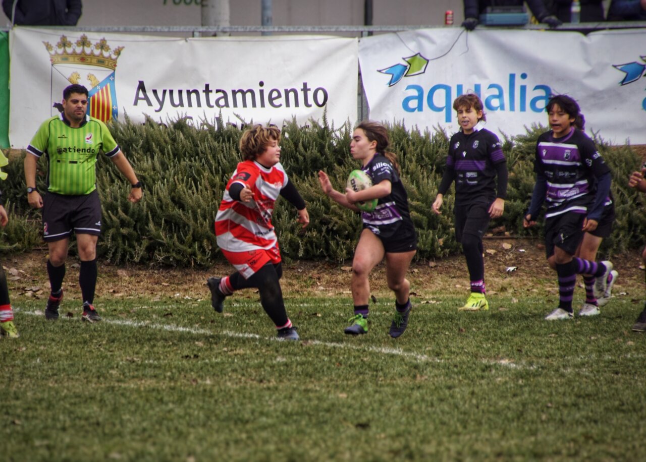 Jugadora sub-14 en un partido de rugby intentando alejar a un contrincante