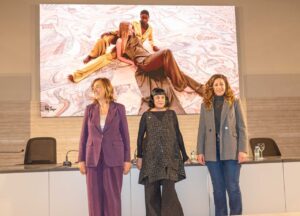 Tres mujeres posando en un evento de moda con un fondo artístico