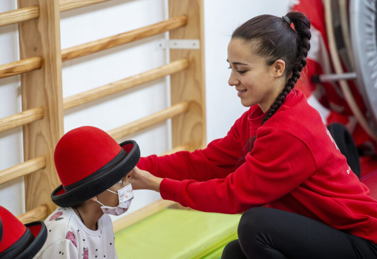 Una mujer coloca un sombrero rojo a un niño en un entorno educativo.