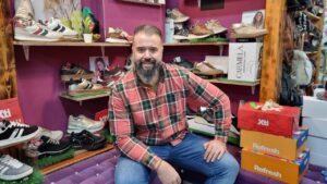 Hombre sonriente en zapatería con calzado variado en estantes