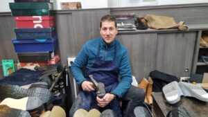 Artesano zapatero trabajando en su taller con herramientas y calzado.