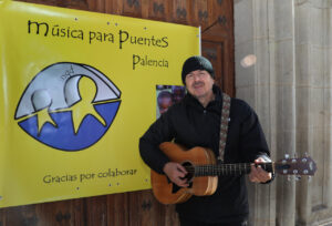 Músico tocando la guitarra frente a un cartel de Música para Puentes