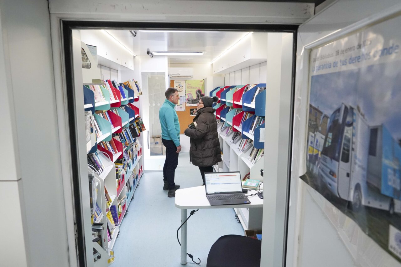 Interior de un bibliobús con libros y usuarios interactuando.