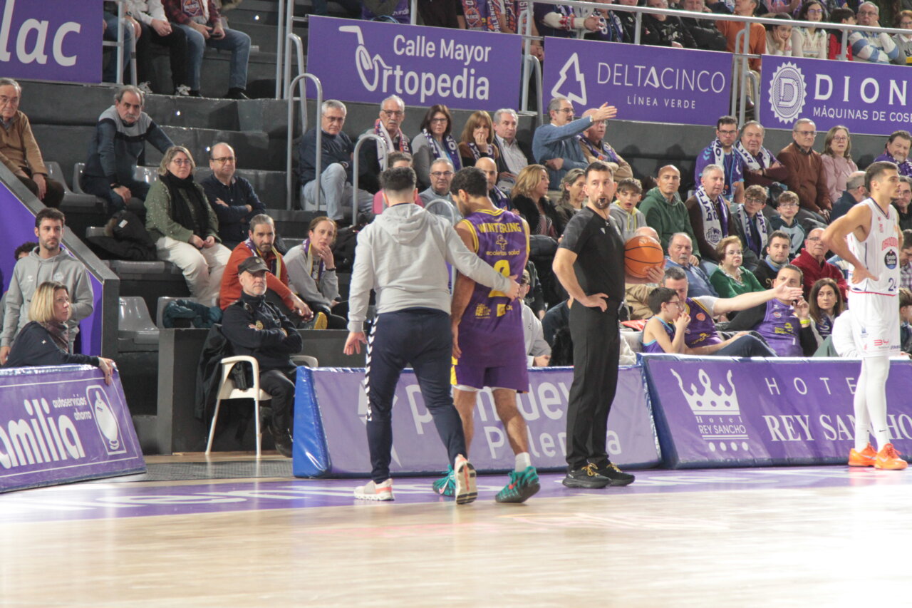 Jugadores de baloncesto en un partido en Palencia con público en las gradas.