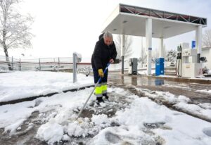 Persona limpiando nieve en una gasolinera durante un aviso amarillo