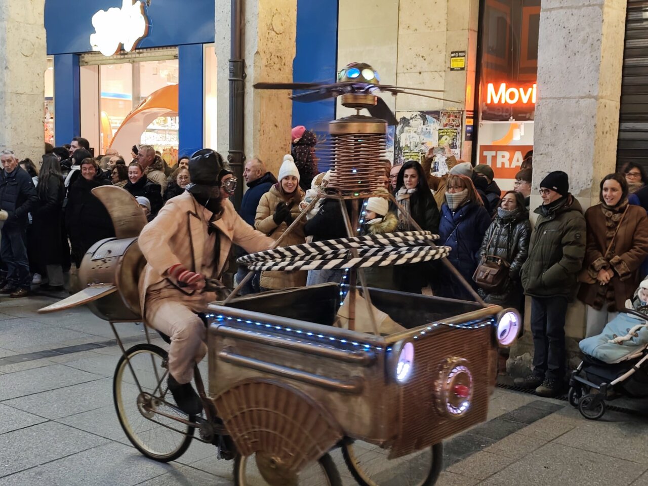 Un artista en bicicleta con un vehículo decorado en la cabalgata de Reyes en Palencia