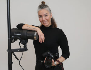 Fotógrafa sonriente sosteniendo una cámara y un equipo de iluminación